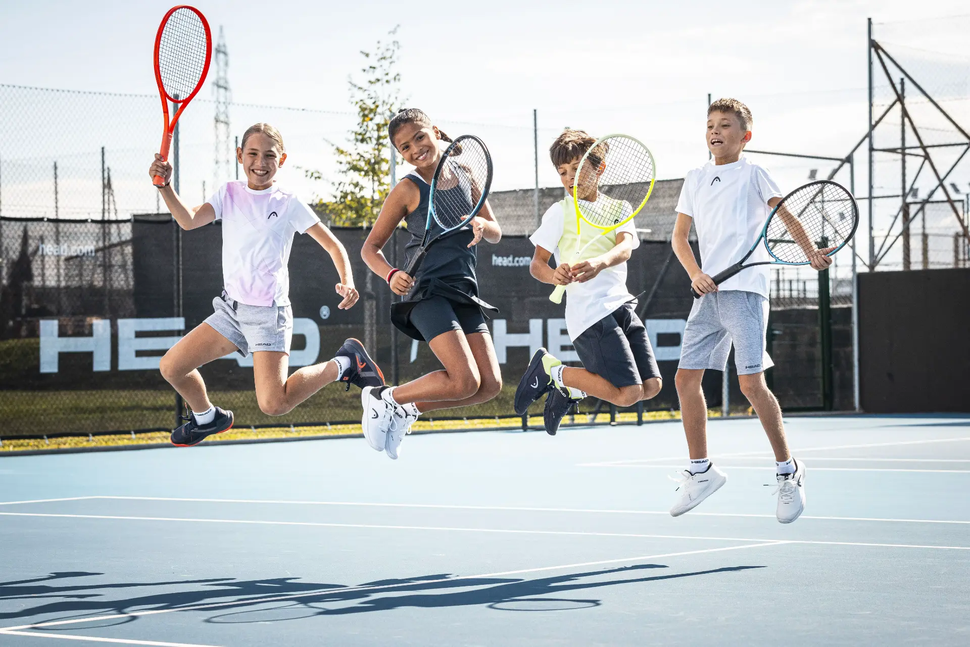 Vier Kinder springen mit Tennisschlägern auf dem Platz während eines Tenniscamps