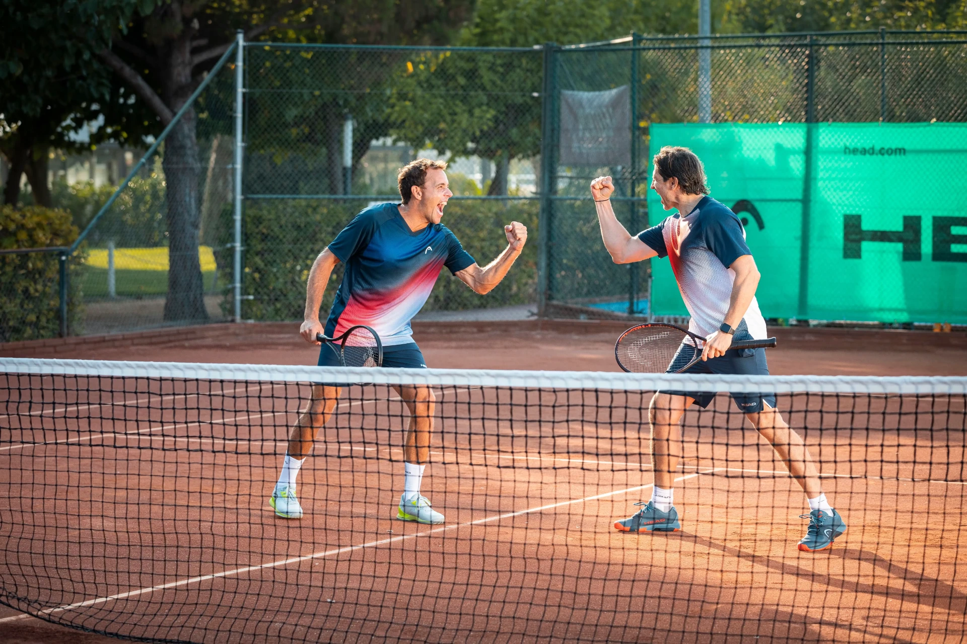 Tennisreise mit M-IDEA Zwei Tennisspieler jubeln nach dem Matchgewinn auf dem Sandplatz während einer Tennisreise